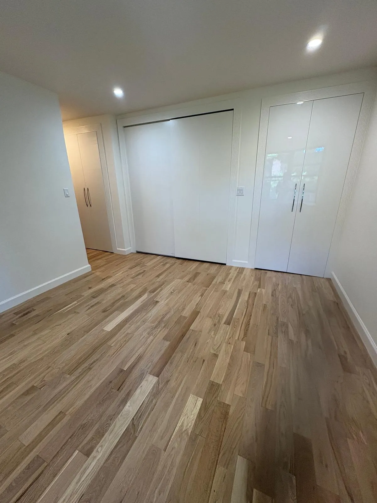 Great Neck bedroom with refinished hardwood floor and custom white closets