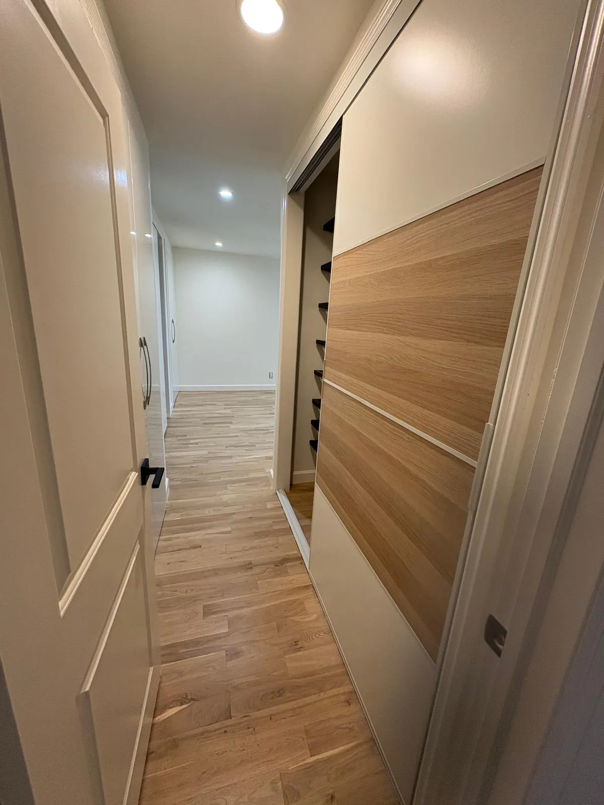 Great Neck hallway with custom wood-panel sliding closets and hardwood flooring