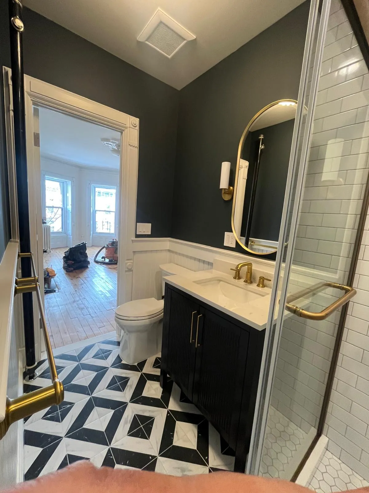 Black vanity with brass fixtures and oval mirror in a Park Slope bathroom