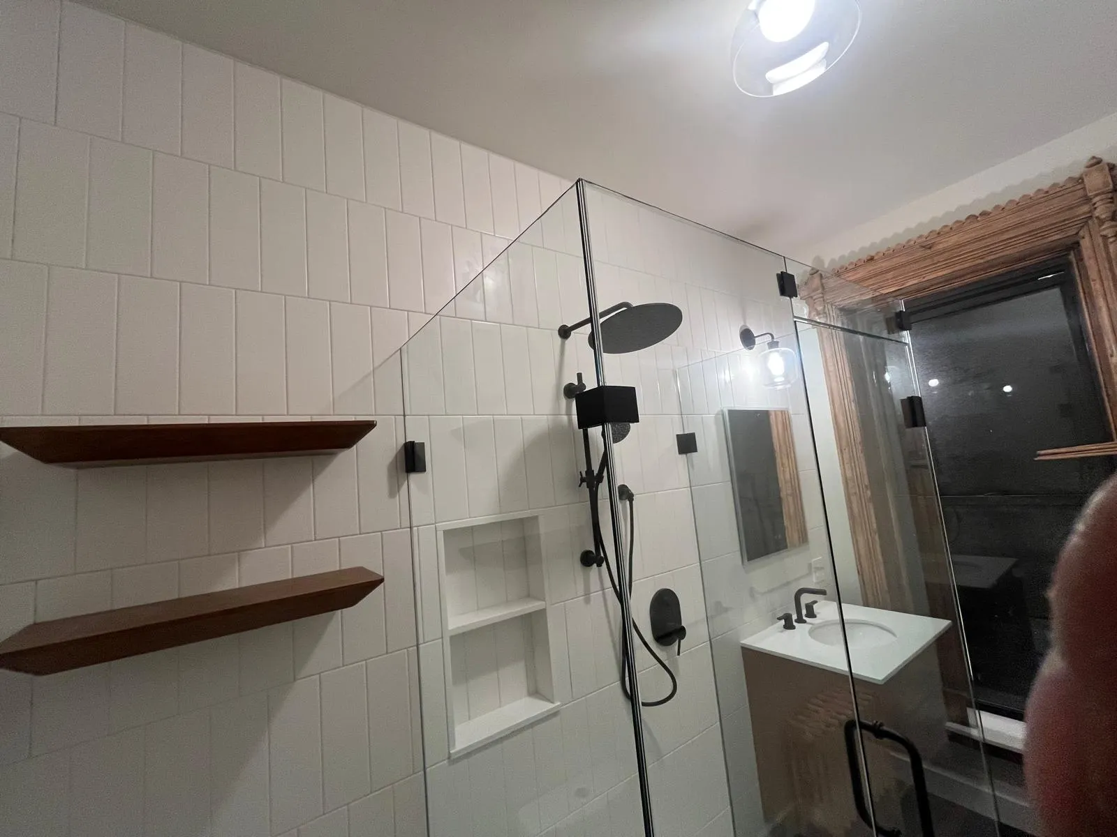 Black rain shower, built-in niche, and wood shelving in a Park Slope bathroom